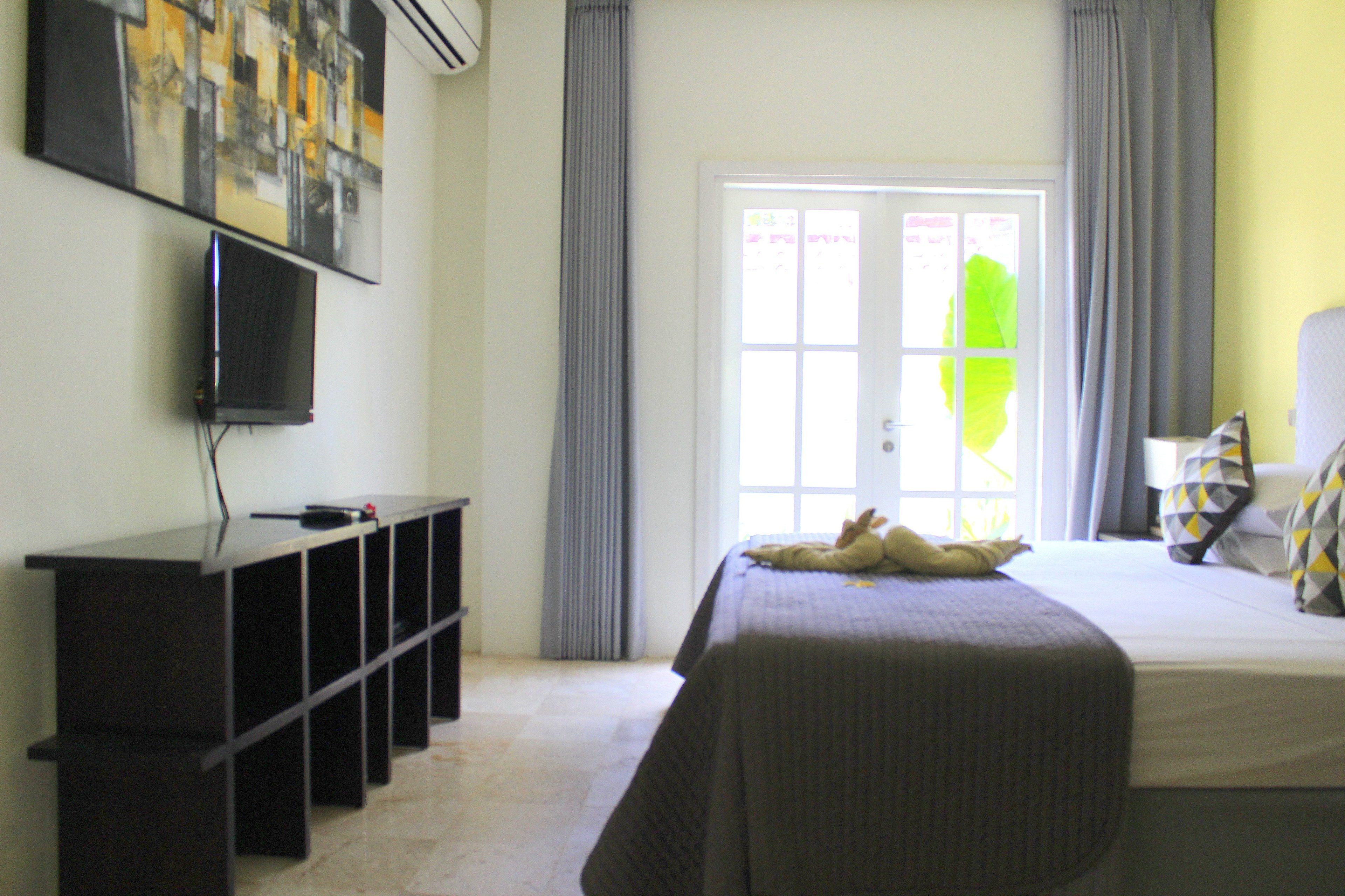 A hotel room with a bed, a TV mounted on the wall, and a window with curtains.