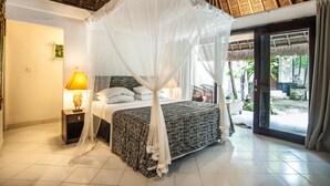 A bedroom with a bed, a nightstand, a lamp, and a view of the outside. - Bali Mystique Hotel and Apartments (Keroboken Kelod)