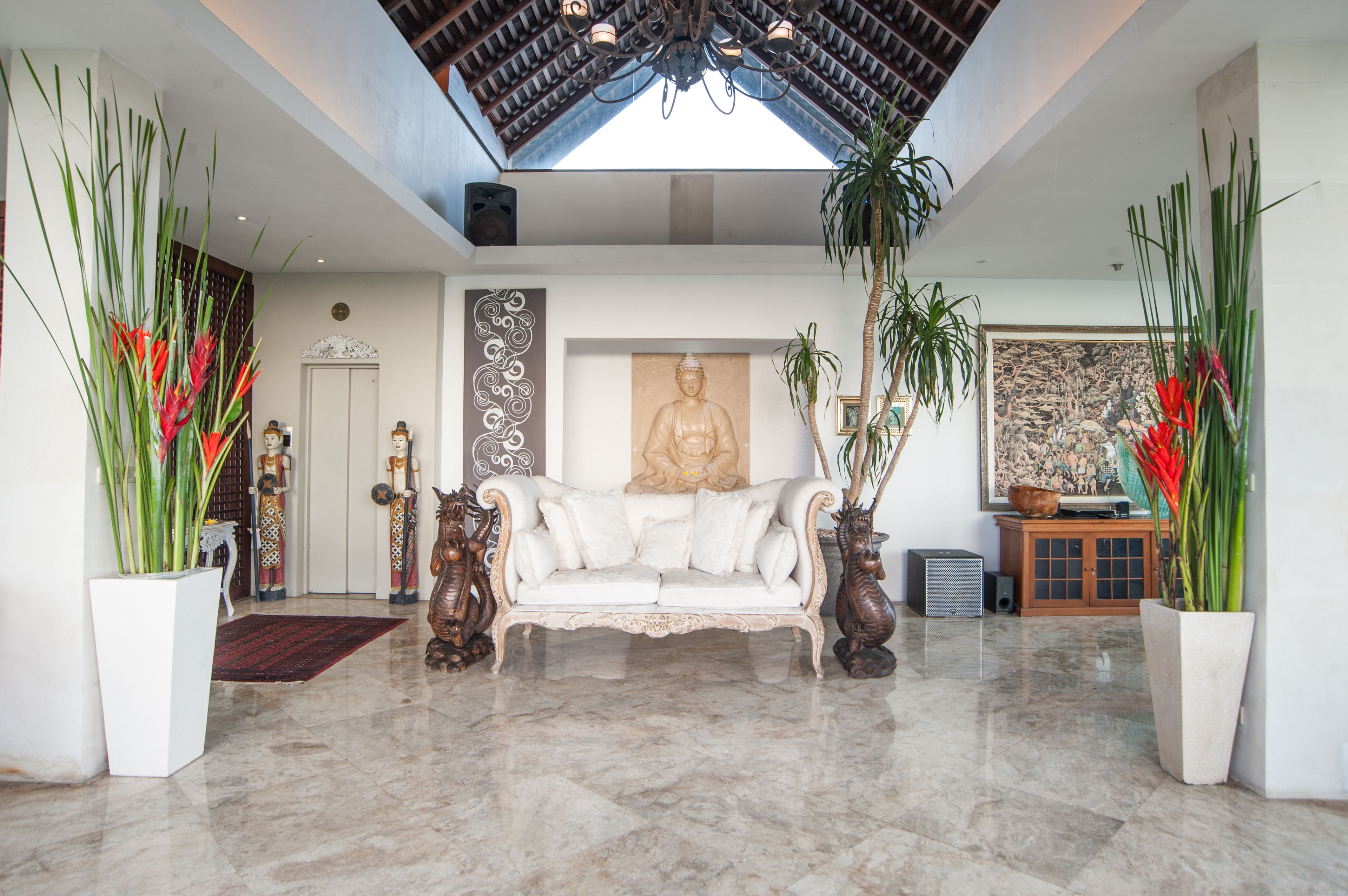 A spacious lobby with a high ceiling, a central white sofa, and large potted plants.