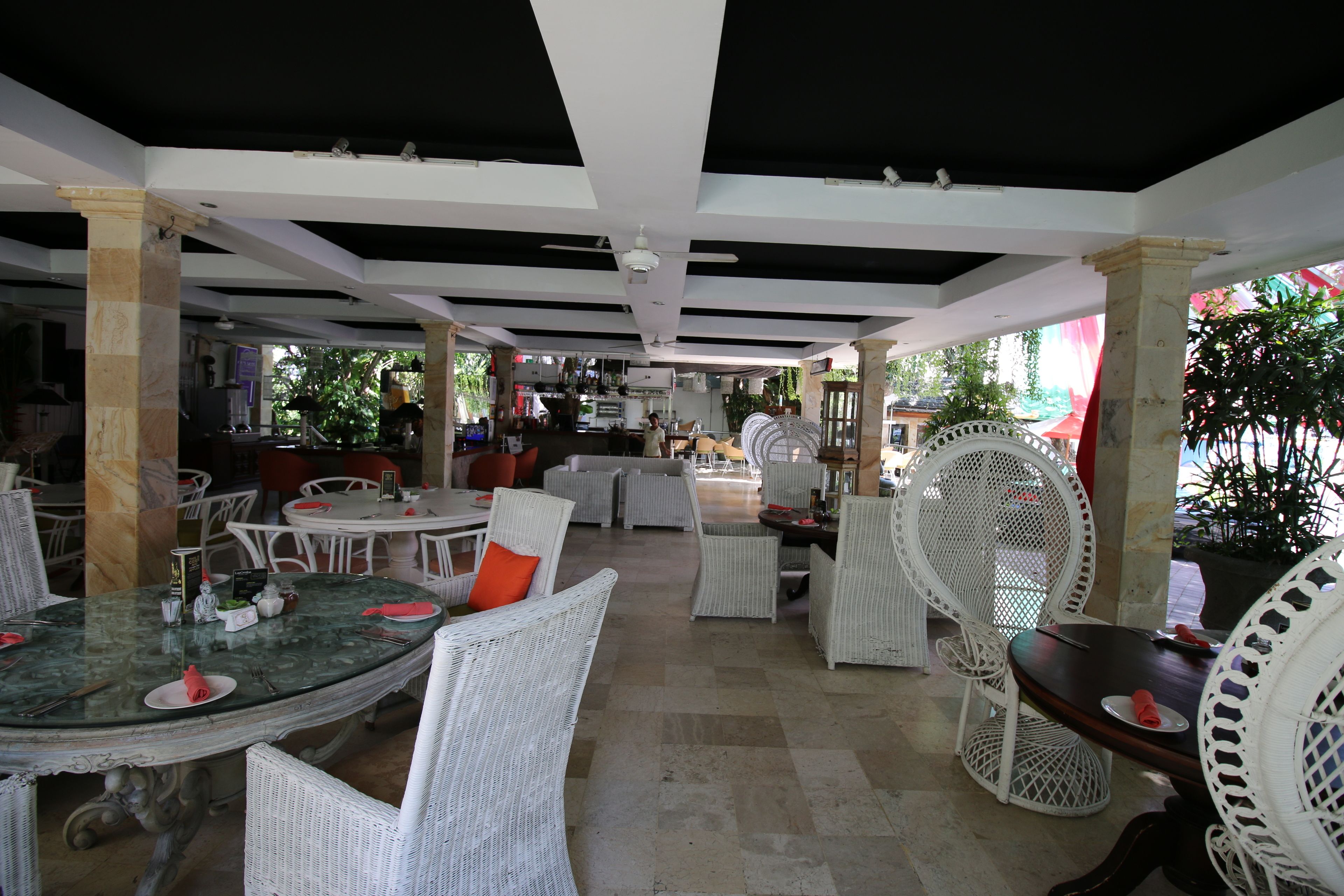 An outdoor dining area with white wicker furniture and a glass table, featuring a ceiling with black beams and a white pillar.