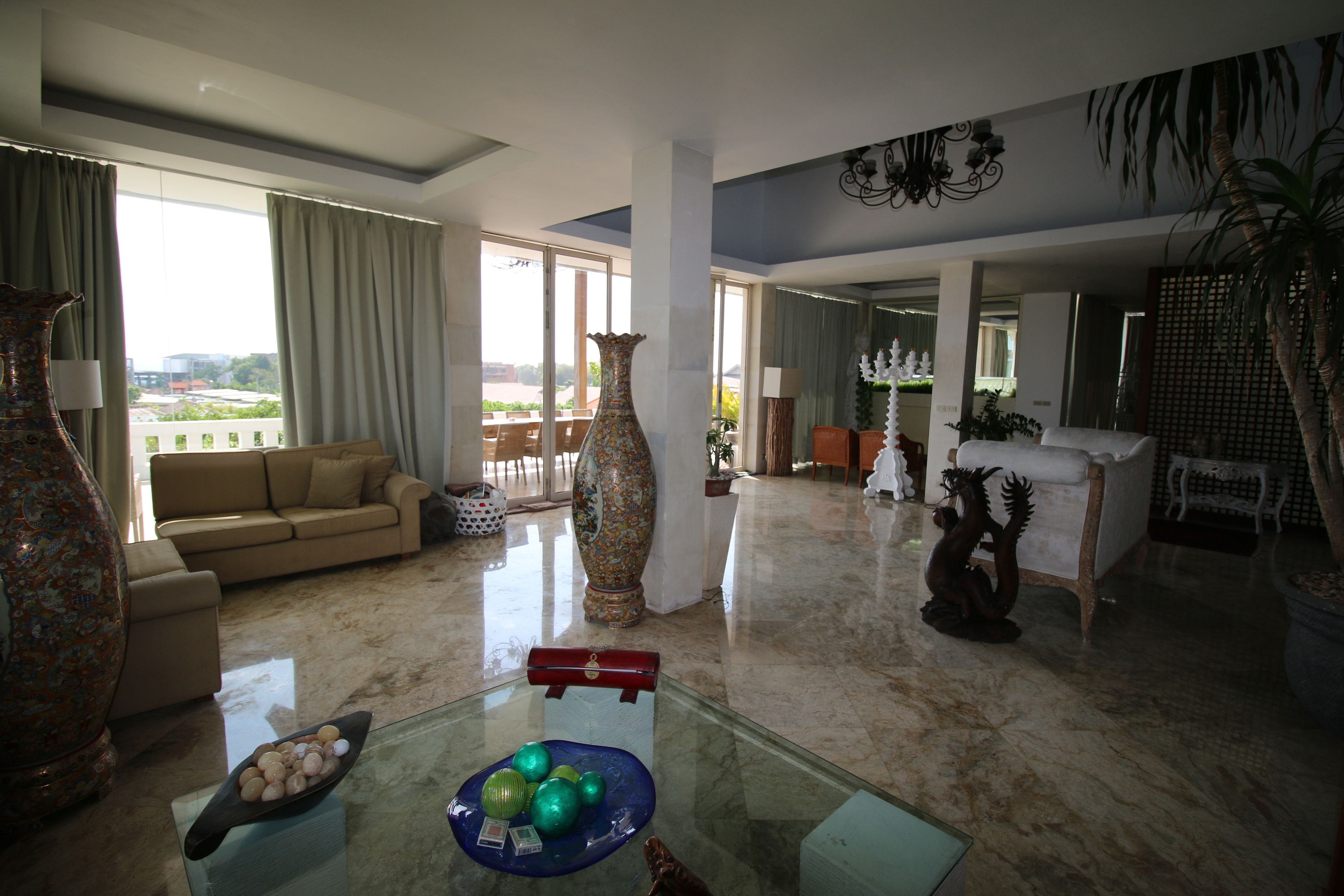 A spacious living room with a large vase, a glass table with decorative items, a sofa, and a view of the outdoors.