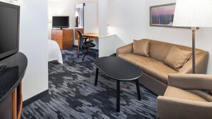 A hotel room with a bed, a sofa, a small table, a TV, a desk with a chair, and a lamp. - Fairfield Inn & Suites Marietta (Marietta)