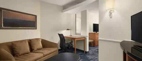 Habitación de hotel con sofá, escritorio, silla, televisión y un cuadro en la pared.