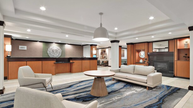 A modern hotel lobby with a round coffee table, sofas, a kitchen area, and a fireplace. - Fairfield Inn & Suites Marietta (Marietta)