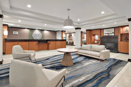 A modern hotel lobby with a round coffee table, sofas, a kitchen area, and a fireplace.