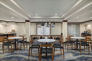 Un comedor de hotel con mesas y sillas redondas, una cocina al fondo y una alfombra estampada.