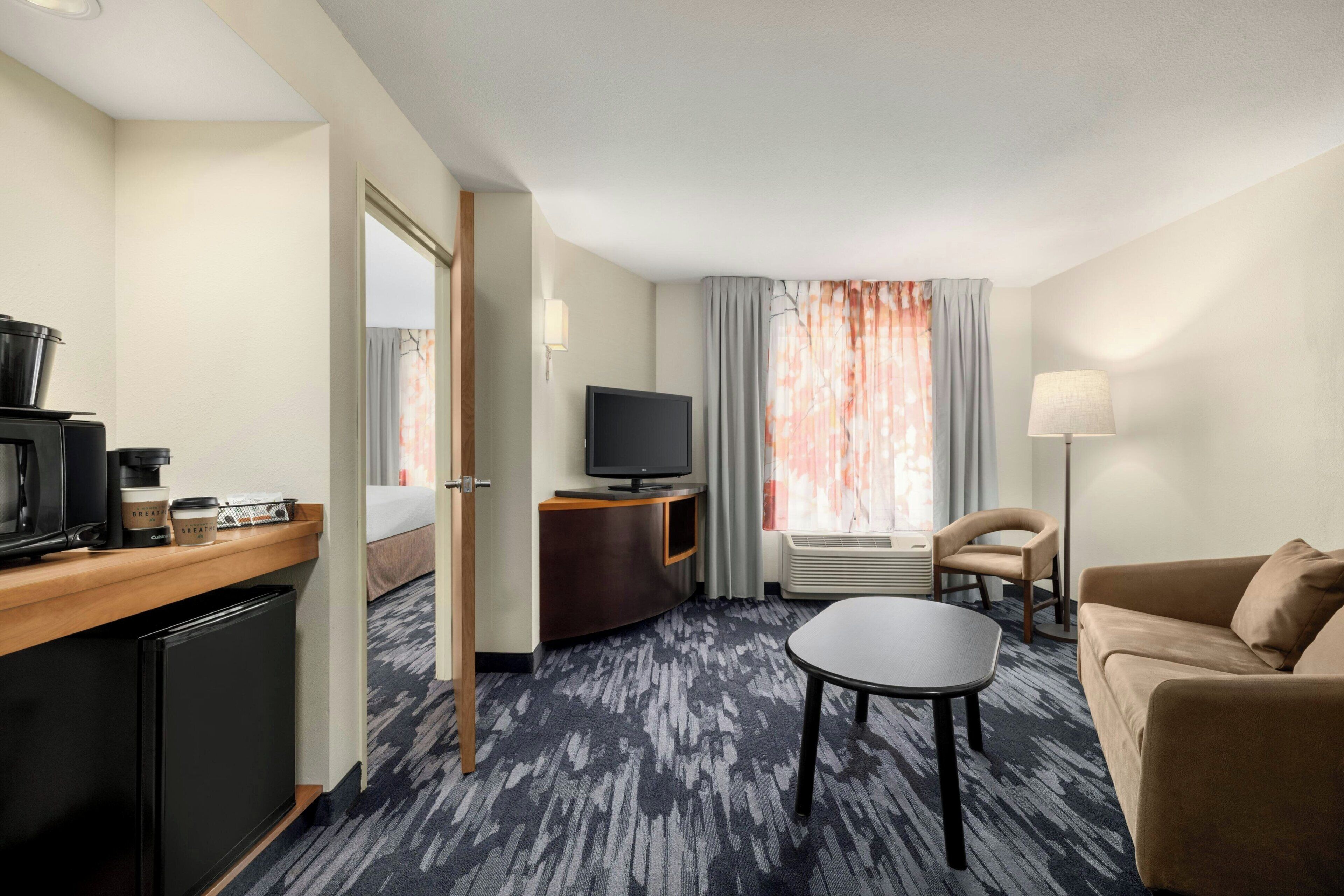 Habitación de hotel con cama, televisión, cafetera, escritorio, silla y sofá.