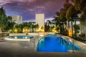A swimming pool area with two pools, surrounded by palm trees and modern buildings.