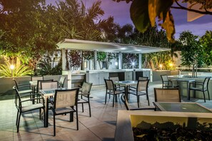 An outdoor patio area with tables and chairs, a bar area, and lush greenery.