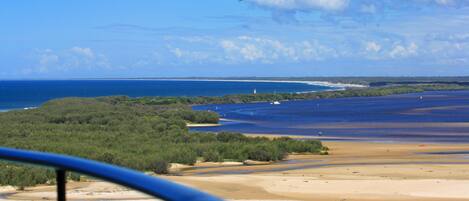 A coastal landscape with a sandy beach, a body of water, and a distant shoreline with vegetation.
