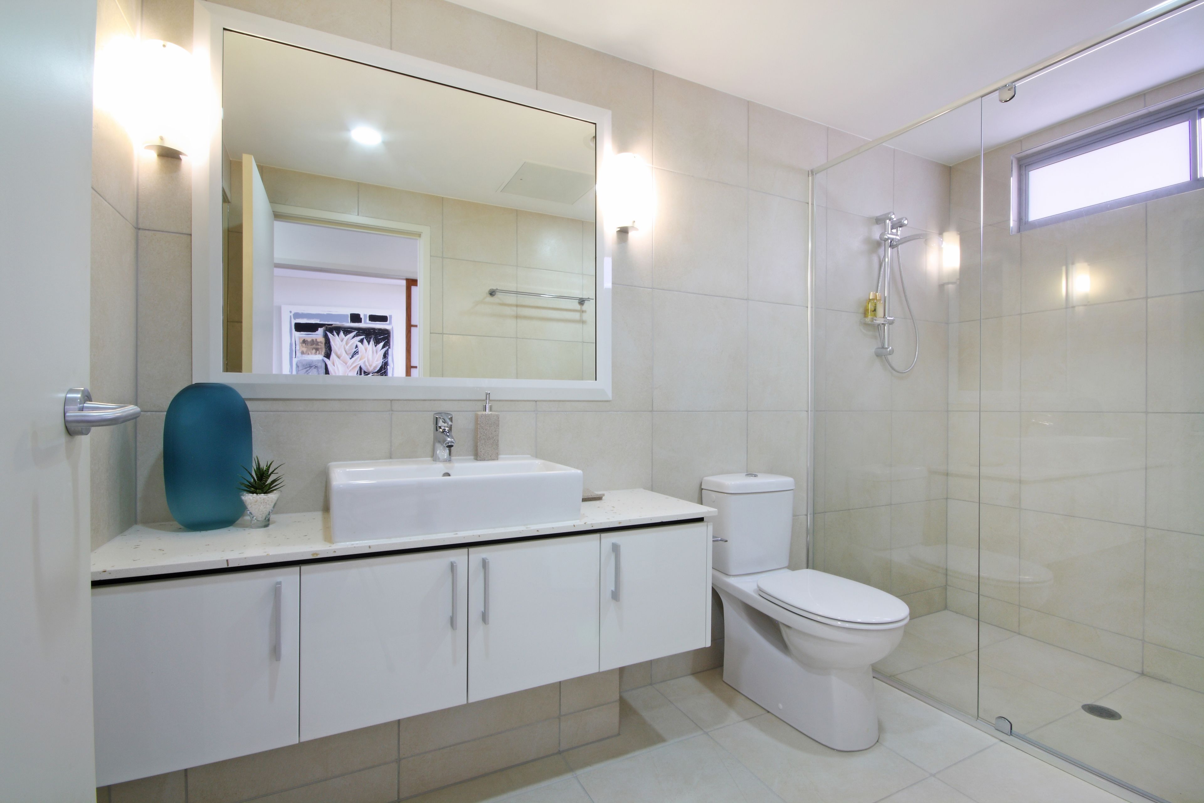 A modern bathroom with a large mirror, white cabinets, a sink, a toilet, and a glass-enclosed shower area.
