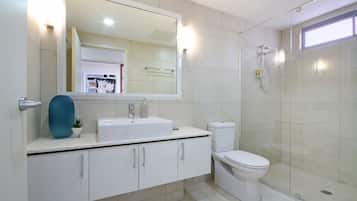 A modern bathroom with a large mirror, white cabinets, a sink, a toilet, and a glass-enclosed shower area.