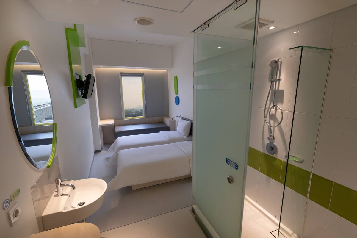 A modern bathroom with a glass shower enclosure, a sink, and a bed with a view of the mountains.