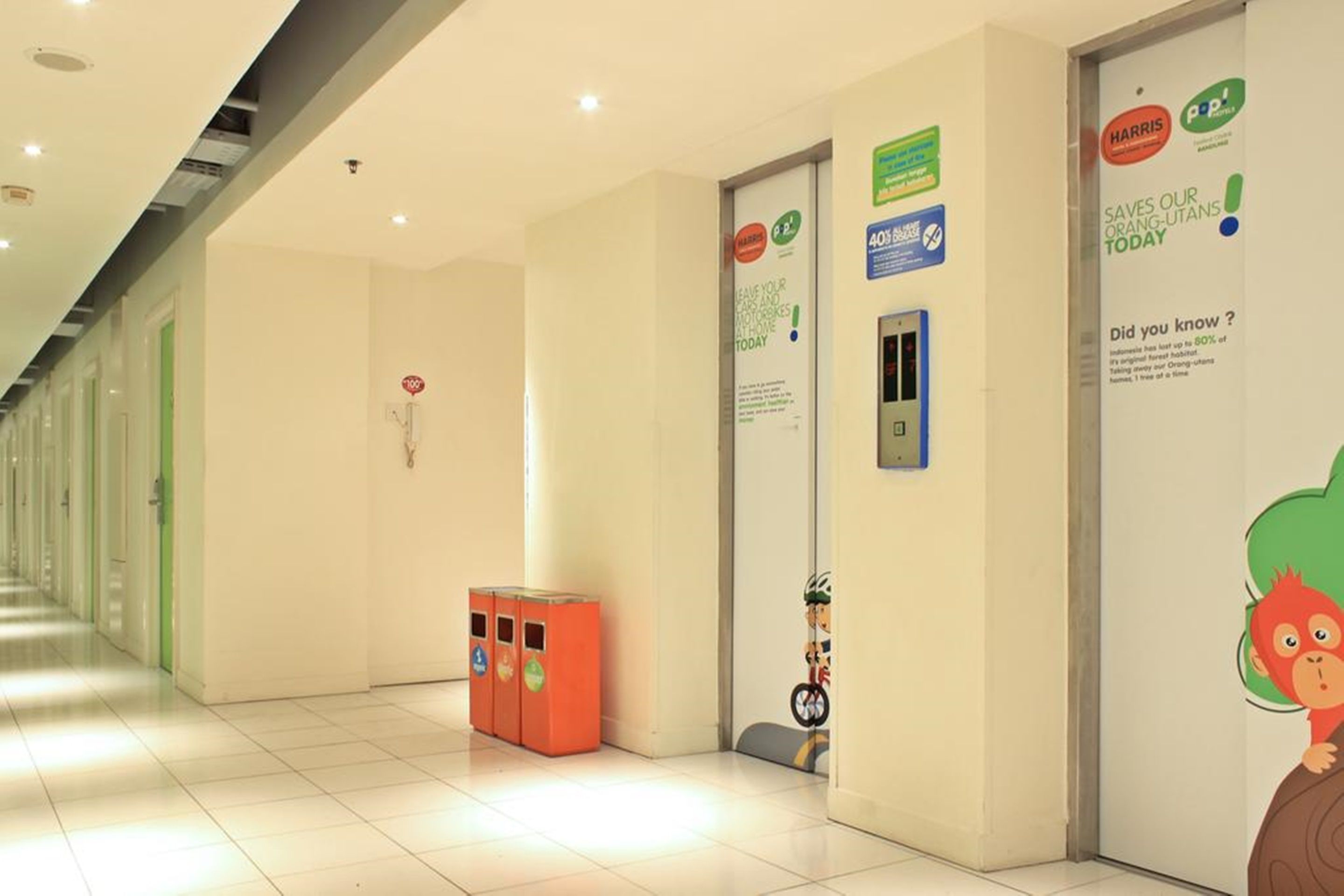 Un pasillo con puertas, un cubo de basura y carteles informativos en las paredes.