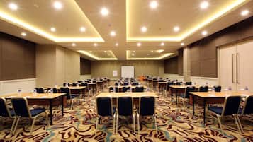 Un salón de conferencias con varias mesas y sillas, equipado con botellas de agua y una pantalla para proyector.