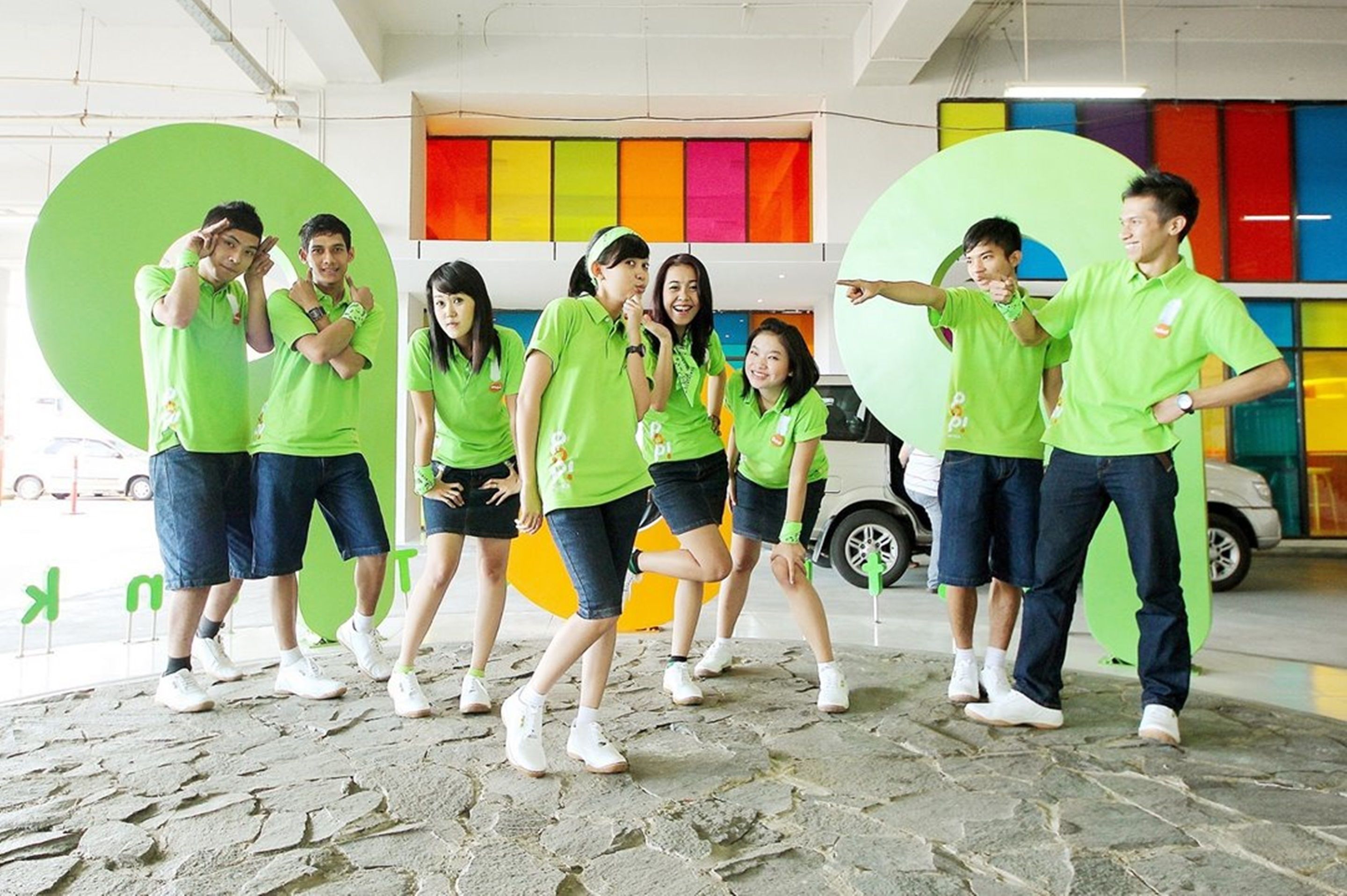 A group of people in green shirts posing in a room with colorful walls and a stone floor.