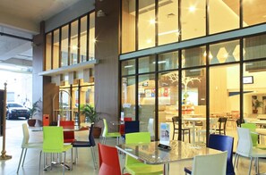 A spacious indoor area with multiple tables and chairs, large windows, and a view of the street outside. - POP! Hotel Festival Citylink Bandung (Bandung)