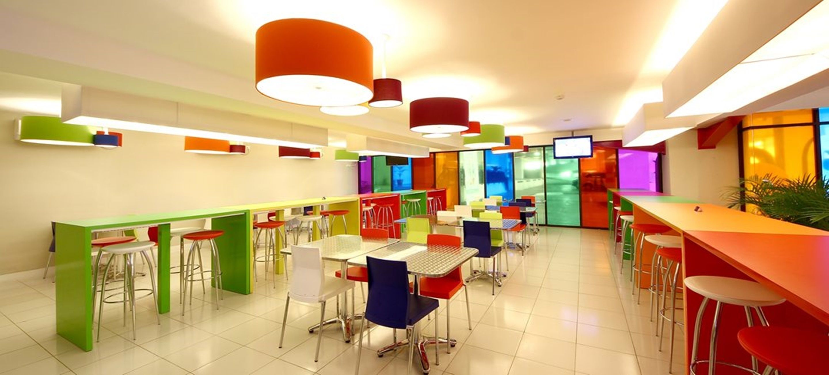 A brightly lit cafeteria with multiple tables and chairs, featuring a modern design with colorful accents.