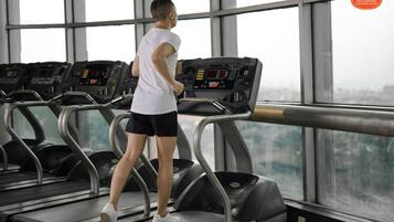 Una persona usando una cinta de correr en un gimnasio con ventanas amplias y varias cintas de correr.