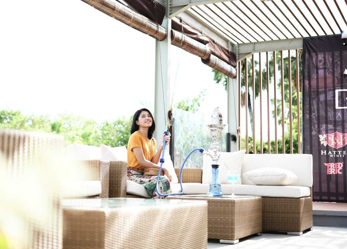 A covered outdoor seating area with wicker furniture, a hookah, and a banner advertising wines.