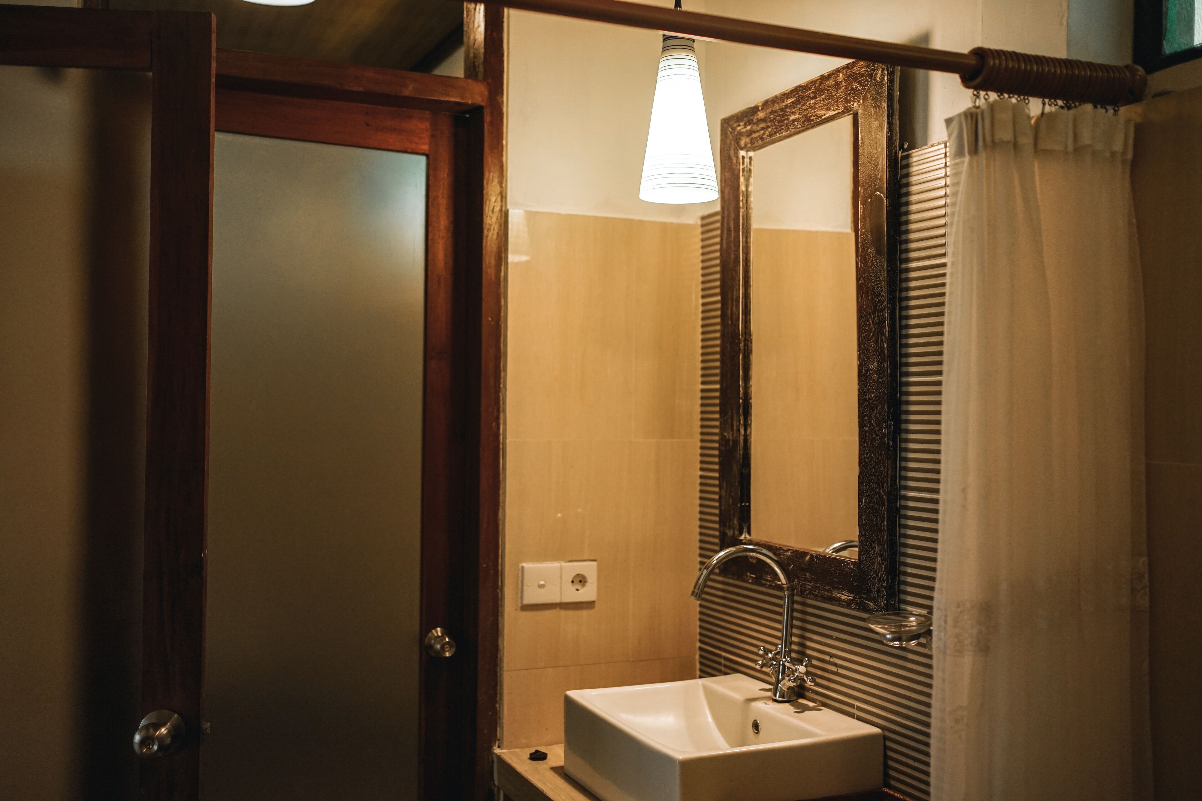 A bathroom with a wooden door, a white sink, a mirror, and a light fixture.