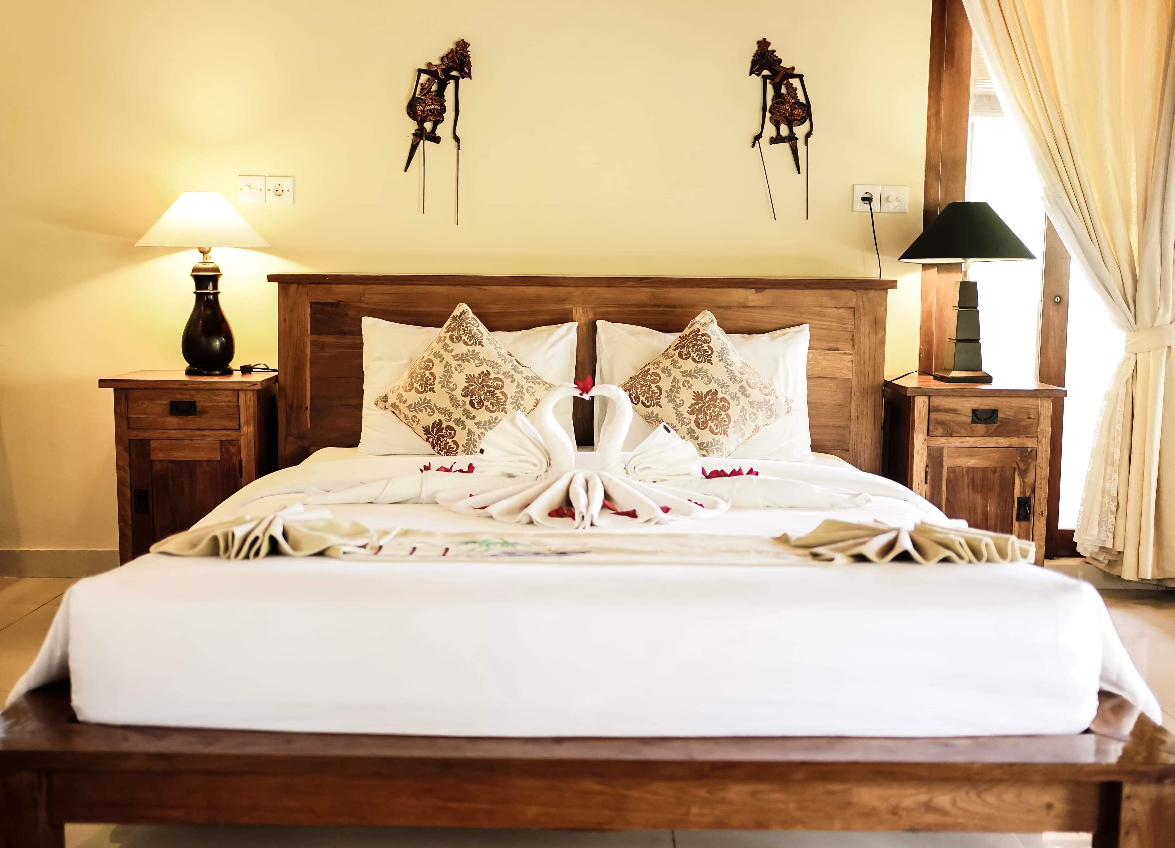Una cama bien hecha con almohadones florales, cabecera de madera y mesitas de noche con lámparas.