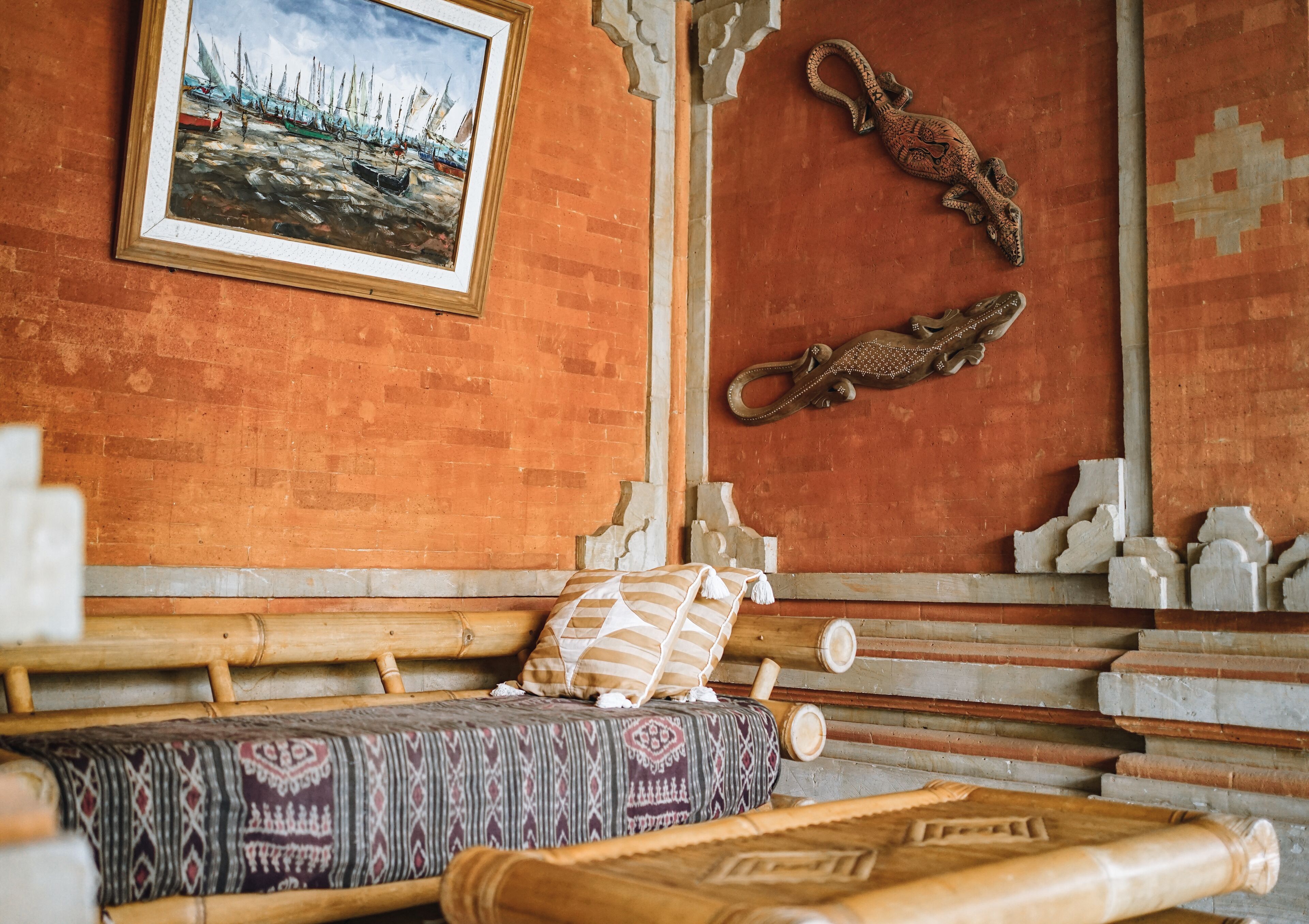 Een klassieke kamer met een houten bed, een kussen met een patroon, een lijstwerk schilderij van boten en decoratieve muursculpturen.