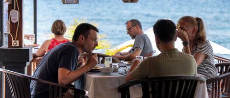 A group of people dining at an outdoor table with a view of the ocean.