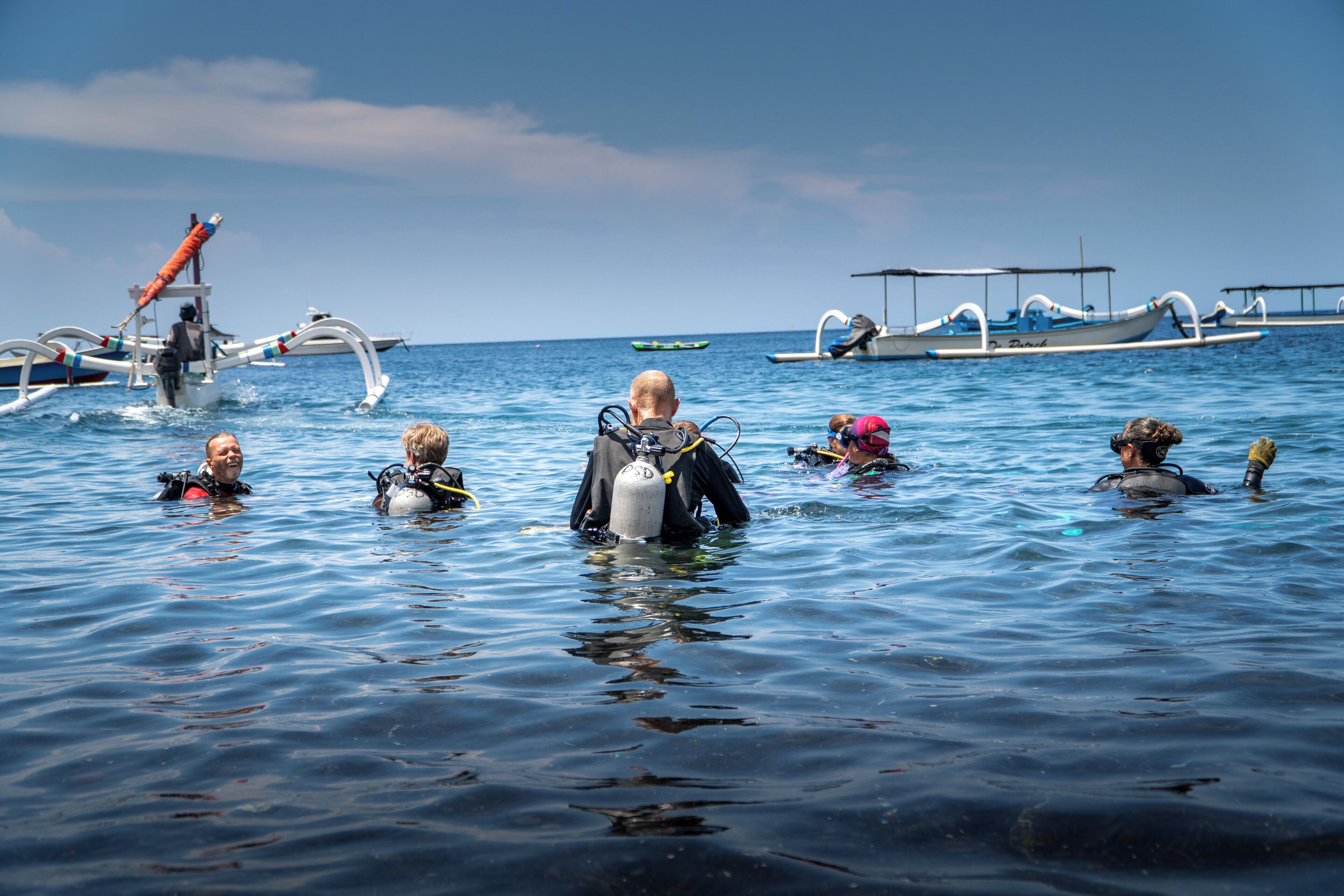 Un groupe de personnes se trouve dans un bateau, dont certains portent de l’équipement de plongée sous-marine, sur une mer calme, avec d’autres bateaux en arrière-plan.