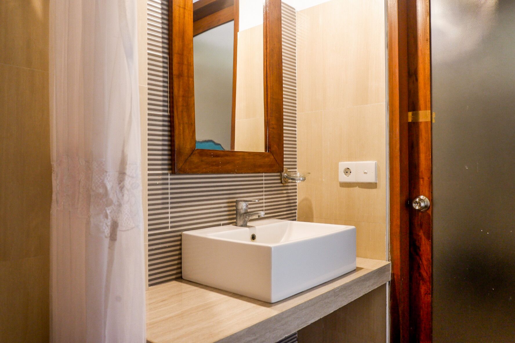 Un baño con un lavabo blanco, puerta de madera y un espejo con marco de madera.