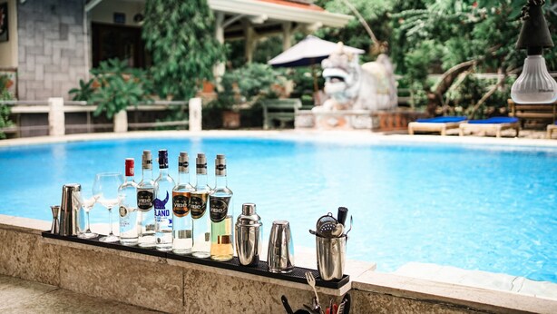 A bar area with a pool in the background, featuring various bottles and bar tools. - Amed Cafe & Hotel Kebun Wayan (Karangasem)