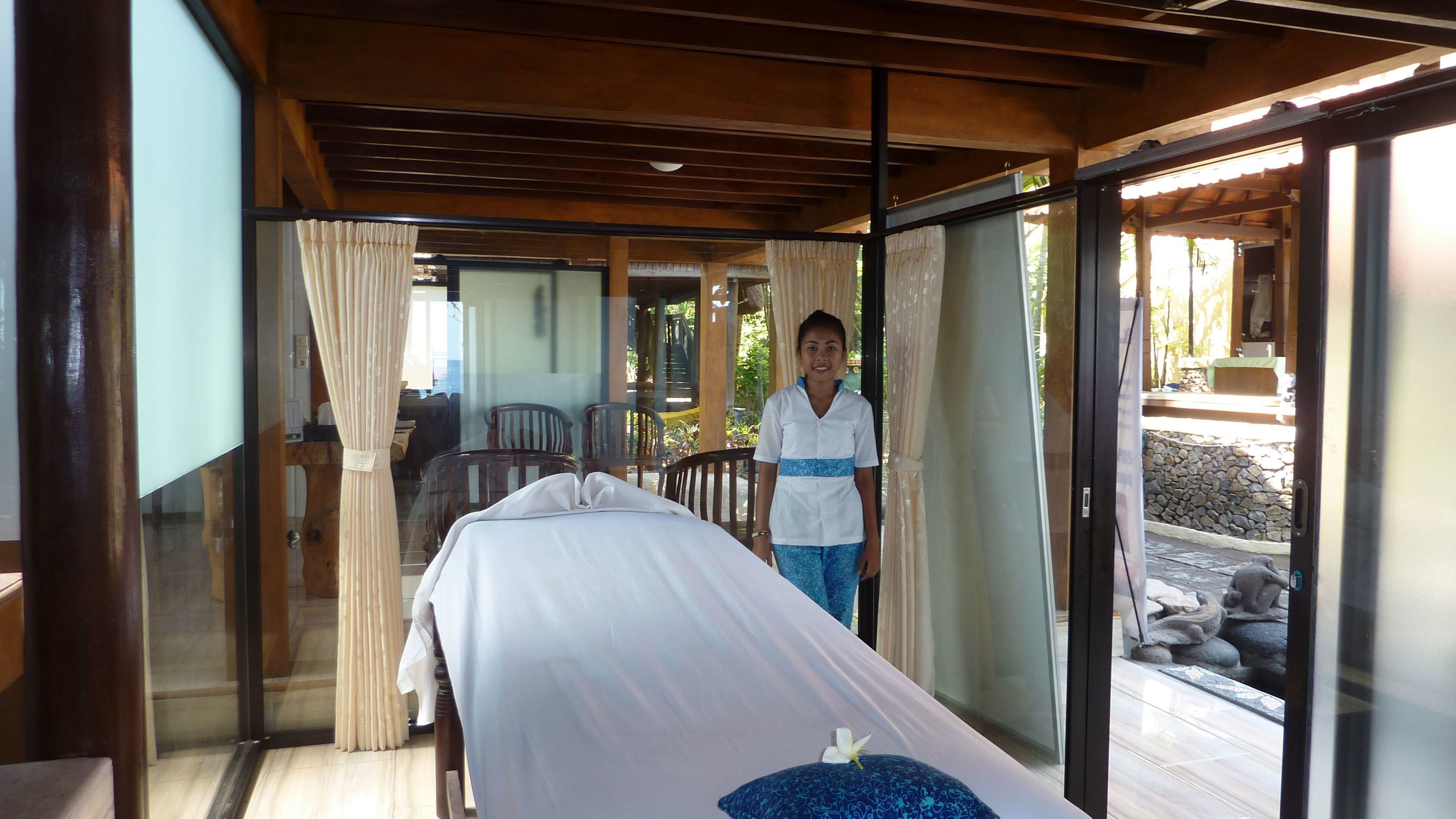 A massage room with a bed, a massage table, and a person standing by the door.