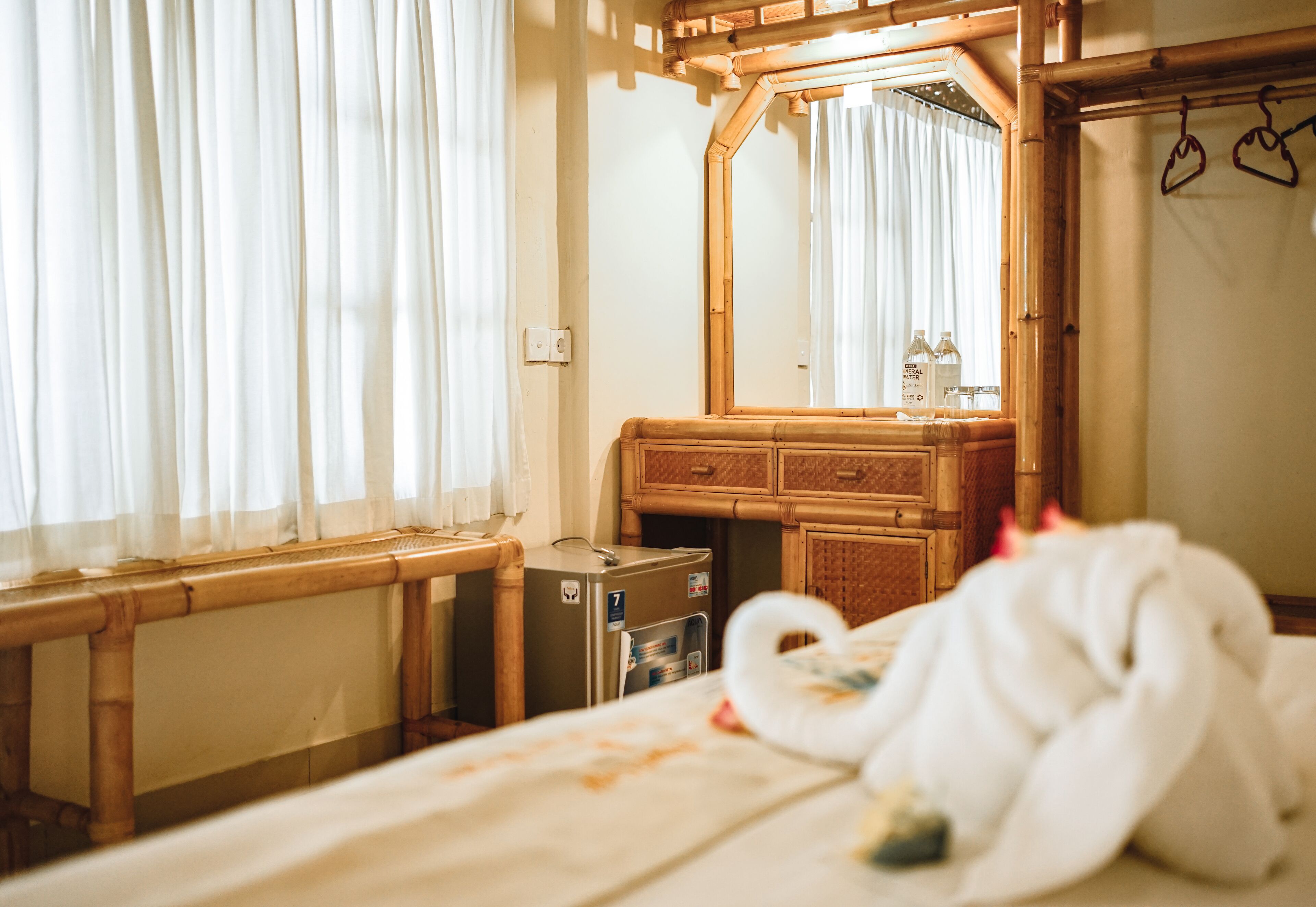 Una habitación de hotel con cama, cómoda de madera, espejo y ventana con cortinas.