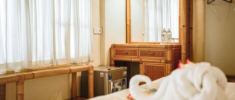 Une chambre d’hôtel avec un lit, une commode en bois, un miroir et une fenêtre avec des rideaux.