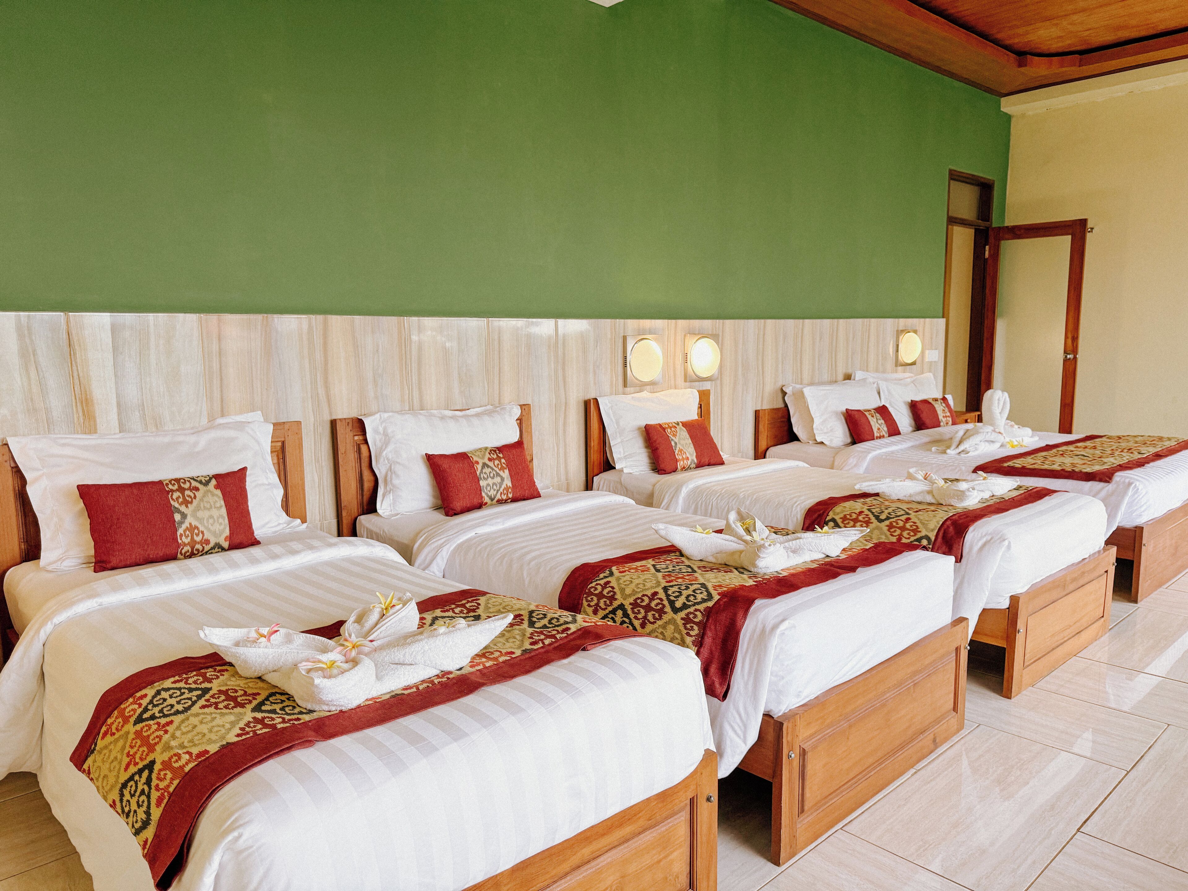A hotel room with four beds, each with white linens and red and beige pillows.