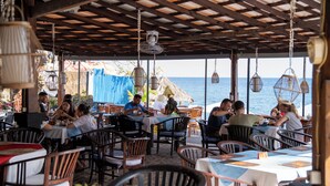 An outdoor restaurant with wooden tables and chairs, hanging lights, and a view of the sea. - Amed Cafe & Hotel Kebun Wayan (Karangasem)