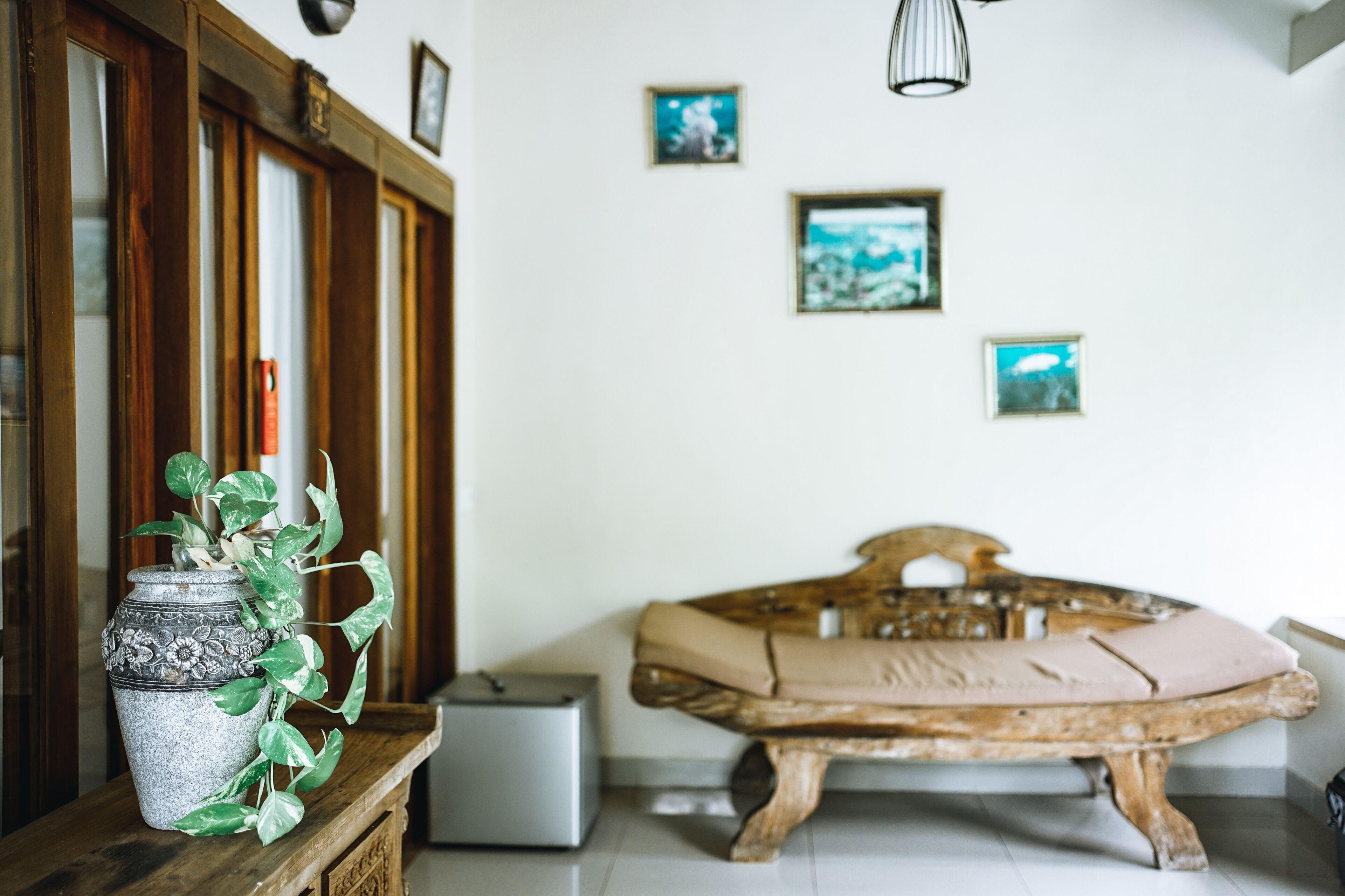 A room with a wooden bed, a small table with a plant, and a wall with framed pictures.