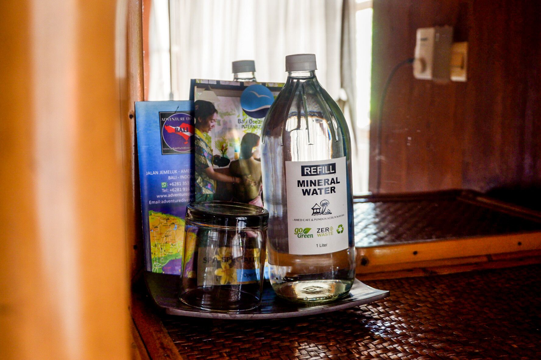 Una mesa con una botella de agua mineral, un tarro de vidrio y un folleto.