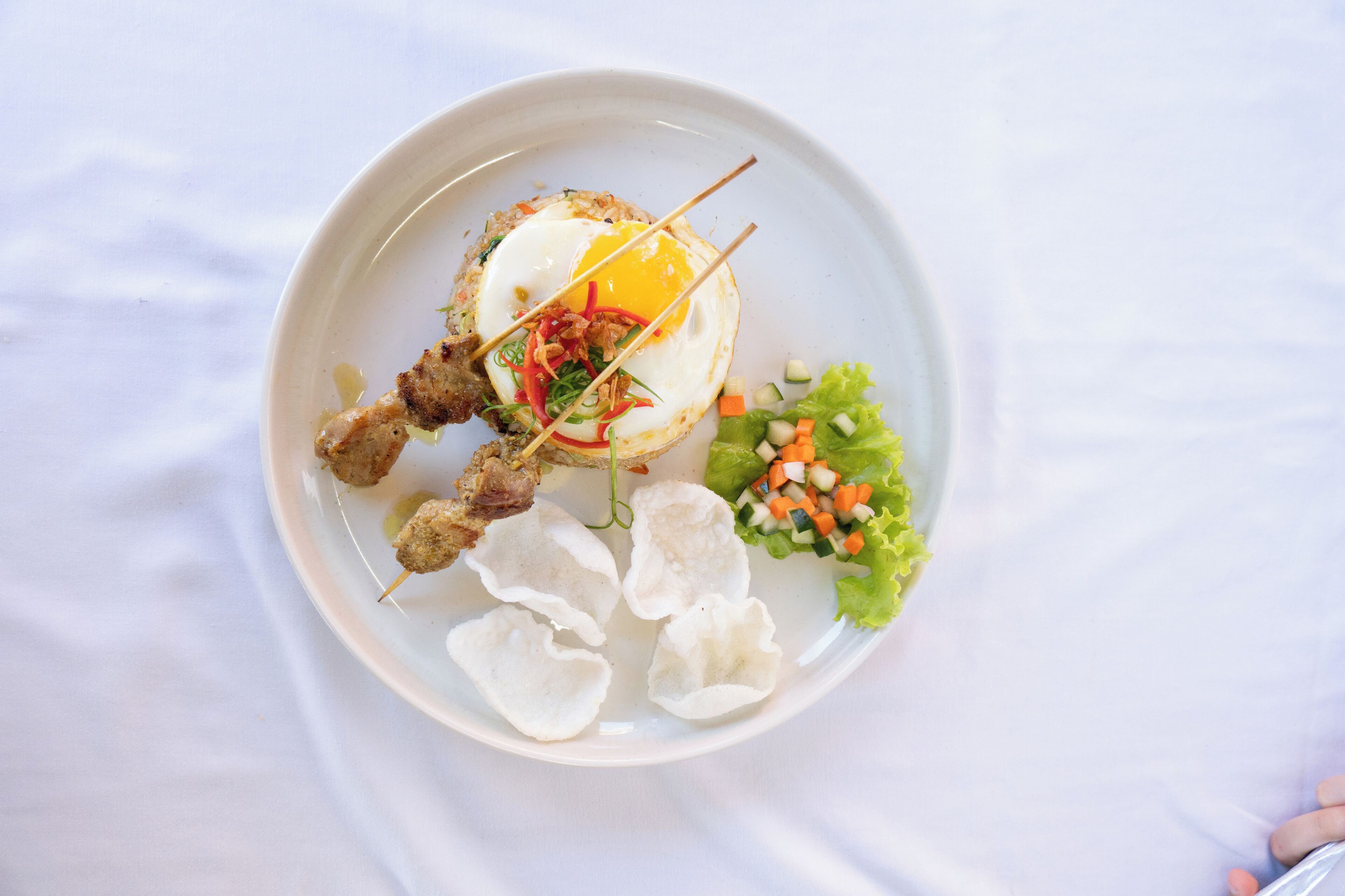 Un plato con un huevo frito, brochetas de carne y una ensalada.