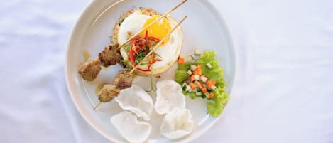 Un plato con un huevo frito, brochetas de carne y una ensalada.