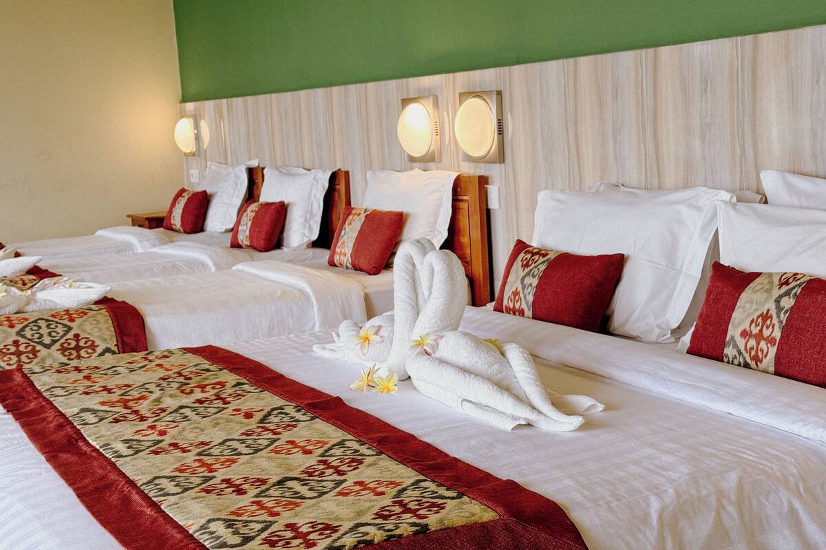 Ett hotellrum med två sängar, båda bäddade med vita lakan och röda och beige kuddar. Det finns handdukar och blommor på sängarna.