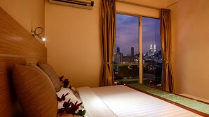 Habitación de hotel con una cama grande, vistas a un paisaje urbano y un equipo de aire acondicionado.