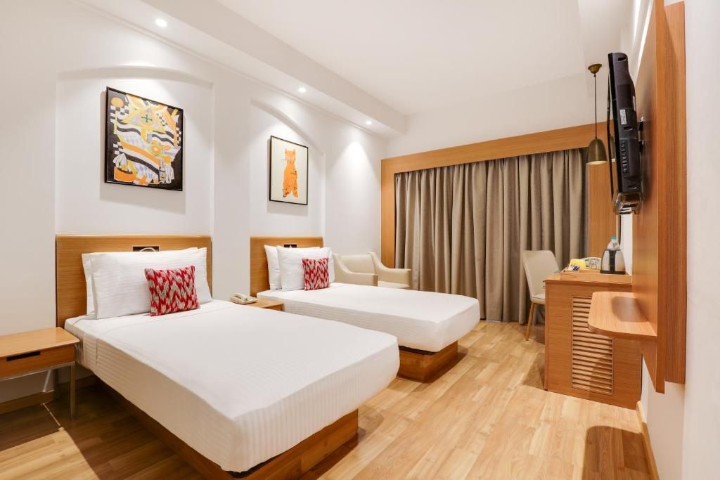 Une chambre d’hôtel avec deux lits, un bureau, une chaise, une télévision et des œuvres d’art accrochées aux murs.