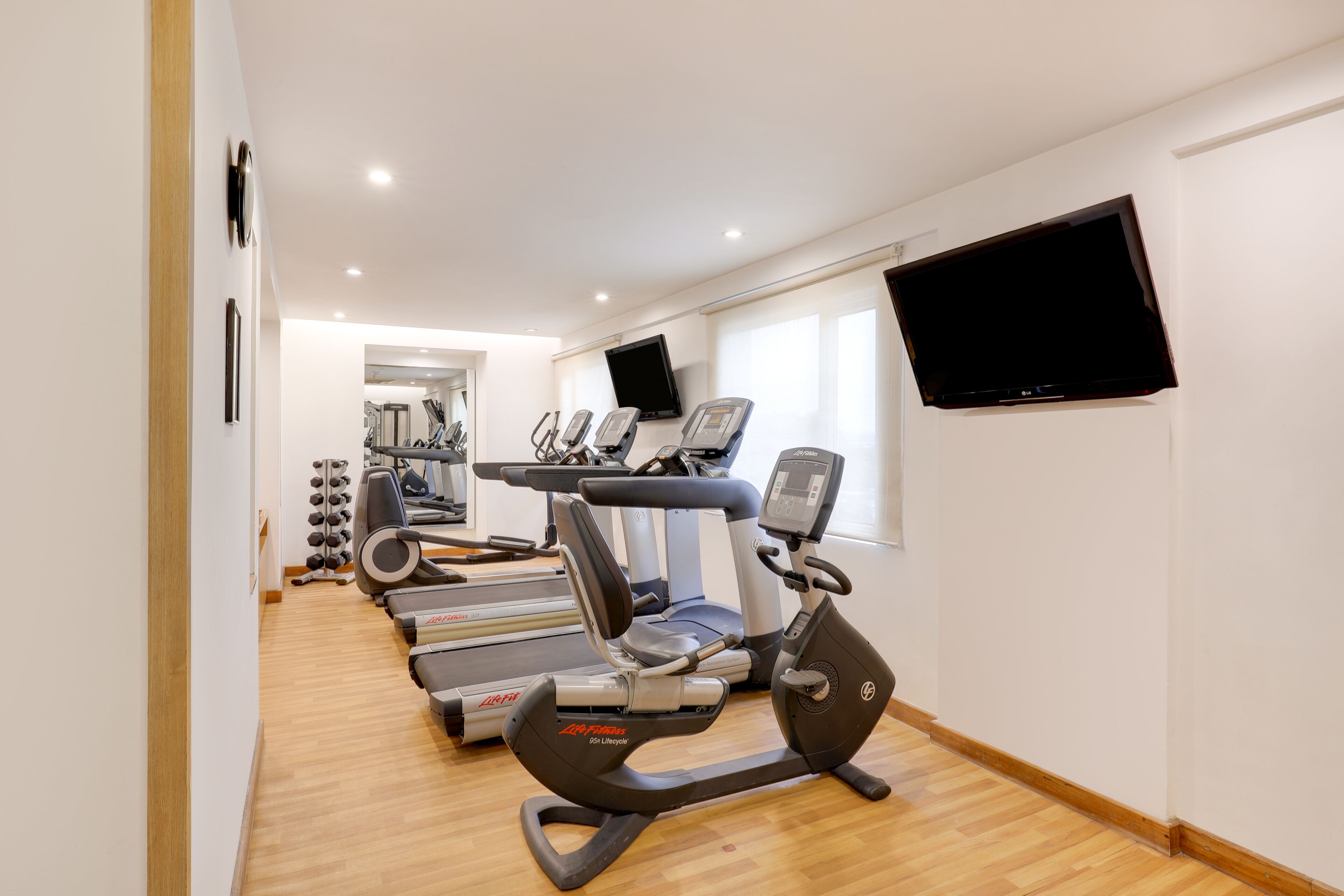 A gym with cardio machines, a TV, and a wooden floor.