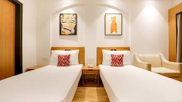 Une chambre d’hôtel avec deux lits, une table de chevet, une chaise et des œuvres d’art accrochées aux murs.