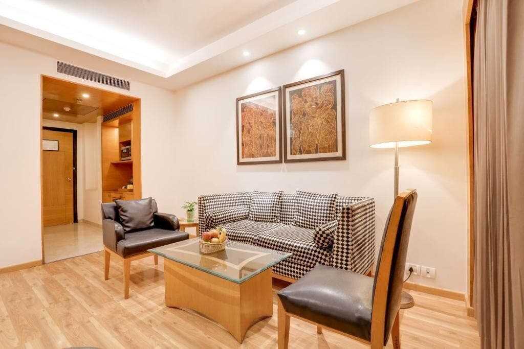 A modern living room with a checkered sofa, a glass coffee table, and a leather armchair. There is a lamp and two framed pictures on the wall.