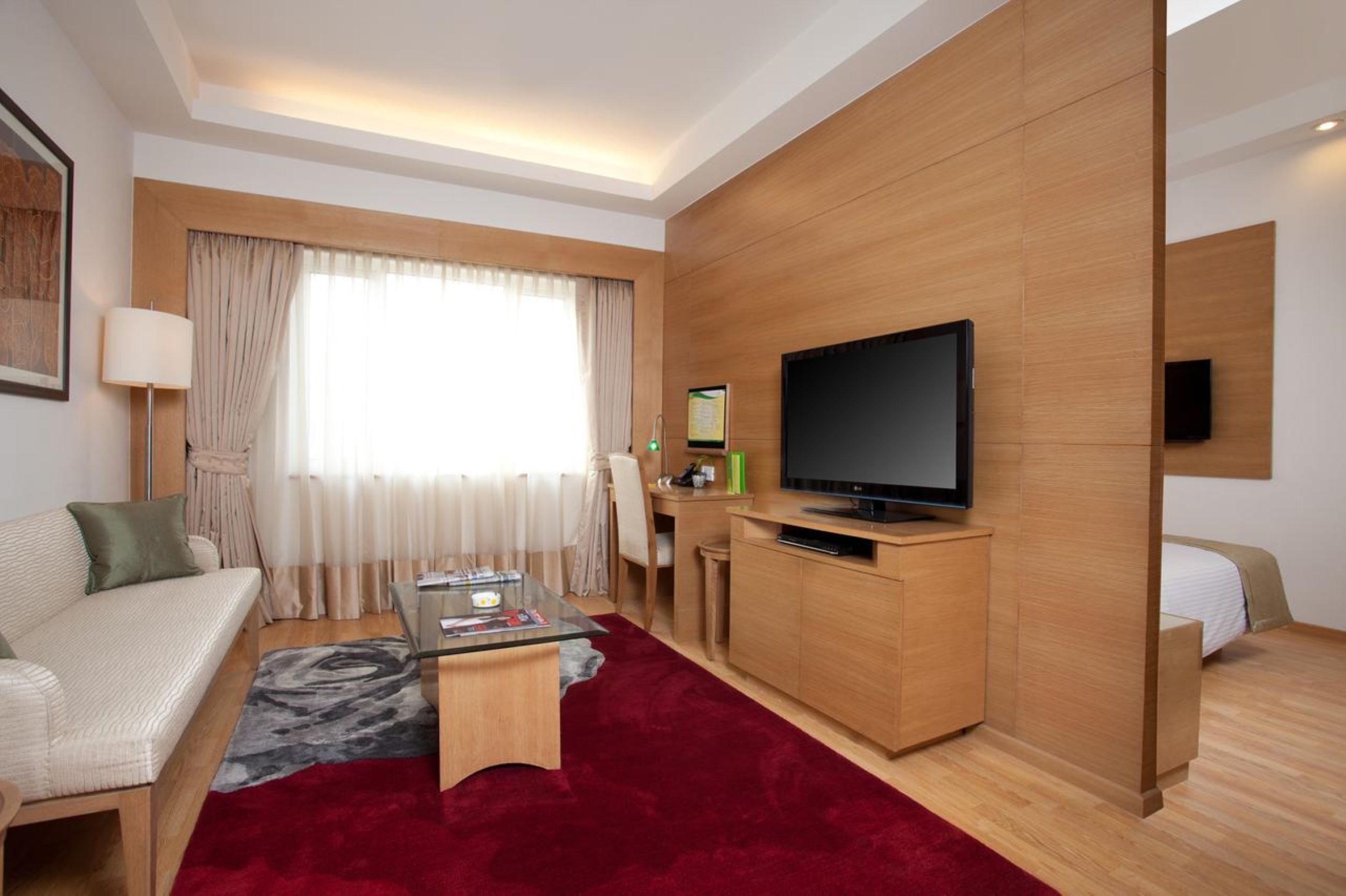 A modern hotel room with a sofa, a glass coffee table, a TV, a desk, and a bed.