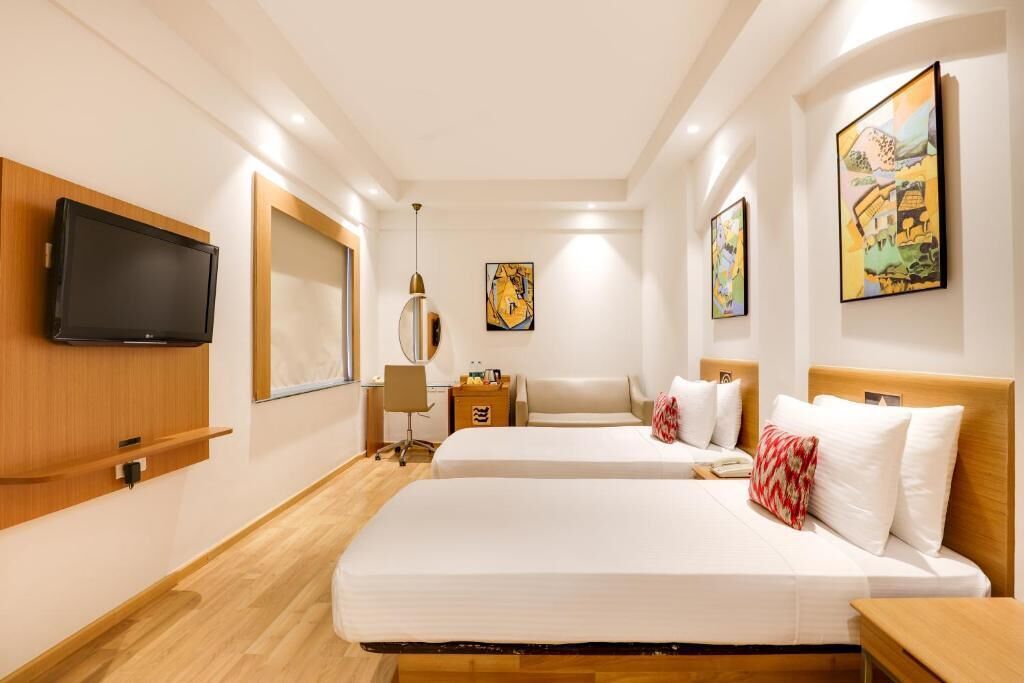 Una habitación de hotel con dos camas, un televisor de pantalla plana, obras de arte en las paredes y piso de madera.