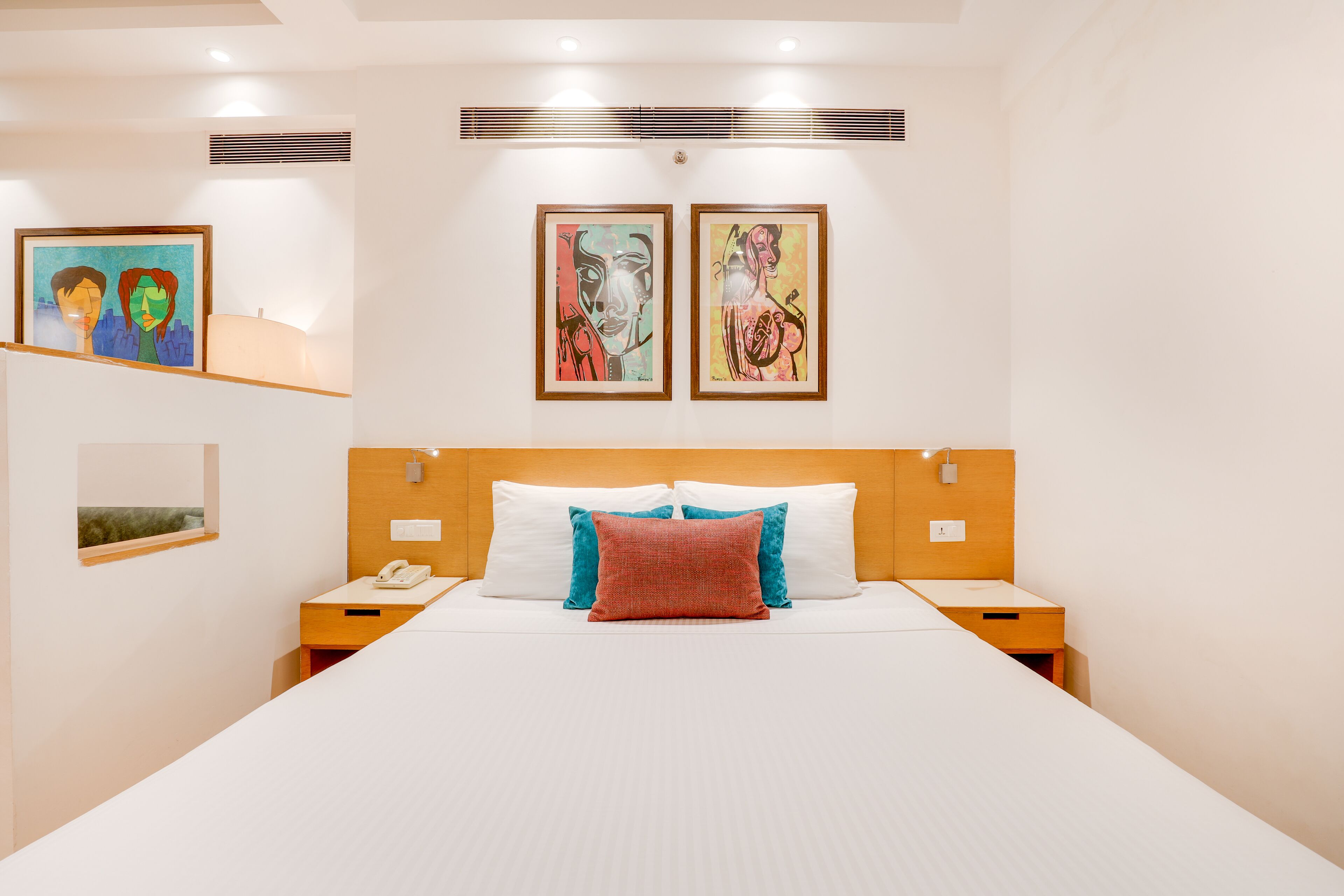 A hotel room with a large bed, two bedside tables, a nightstand, and two framed artworks on the wall.