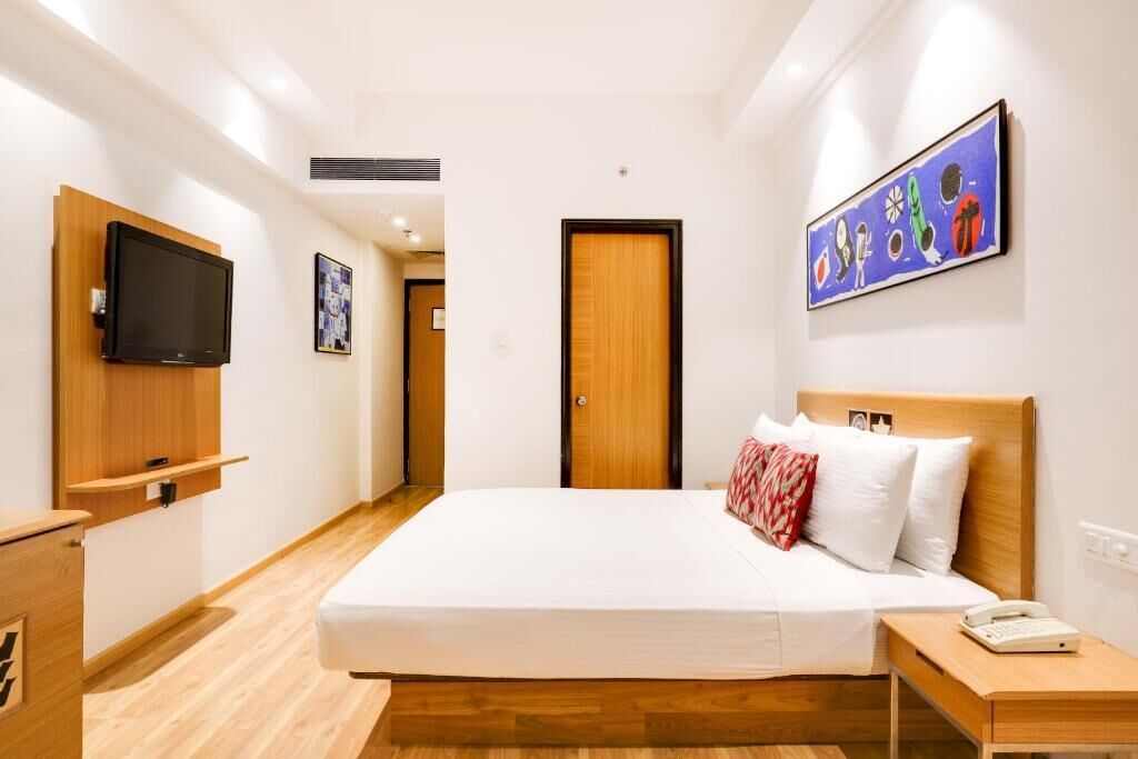 A hotel room with a bed, bedside table, a television mounted on the wall, and a door.